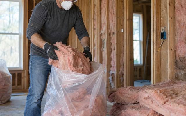 Worker packing old pink batts into a large clear bag during attic insulation removal