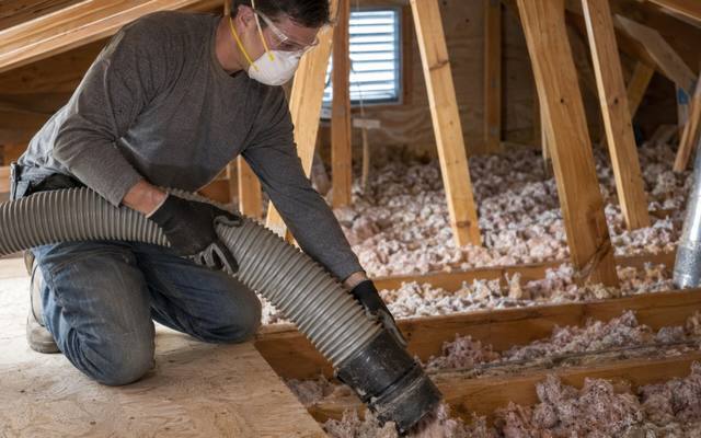 Large vacuum hose pulling old pink loose-fill from between attic joists during blown-in insulation removal