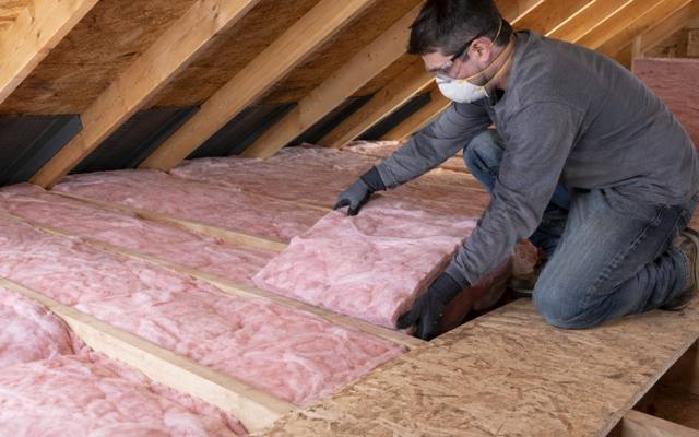 Worker kneeling on an attic floor handling pink fibreglass batts for damaged insulation removal