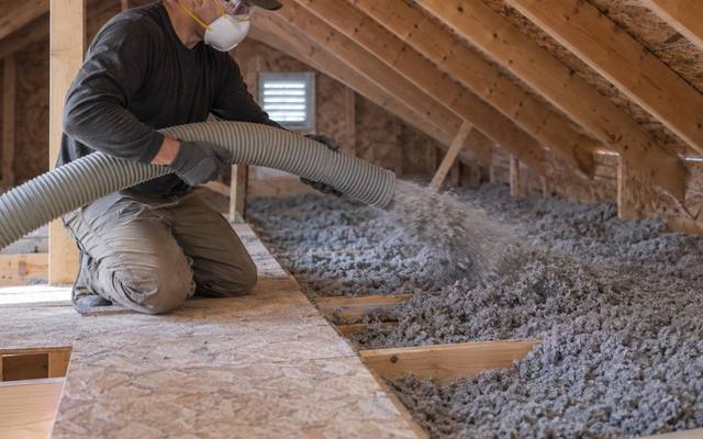 Worker blowing new loose-fill insulation along an attic walkway after insulation removal in Tillsonburg