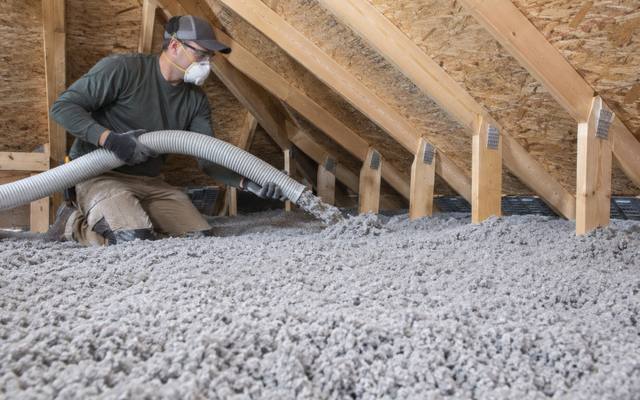 Worker with a hose over a deep, even layer of grey loose-fill covering an attic floor